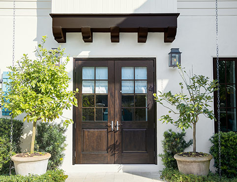 A stucco home with wooden doors and trellis. Bushes and trees adorn the lawn. A stucco home with wooden doors and trellis. Bushes and trees adorn the lawn.